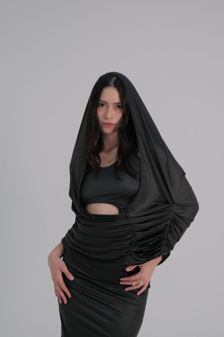 Confident pose in black midi dress with dramatic hood and cutout waist